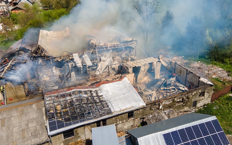 Aerial view of ruined building on fire with collapsed roof and rising dark smoke contra expertise